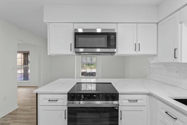 kitchen with light stone counters, stainless steel microwave, range with electric stovetop, and white cabinetry