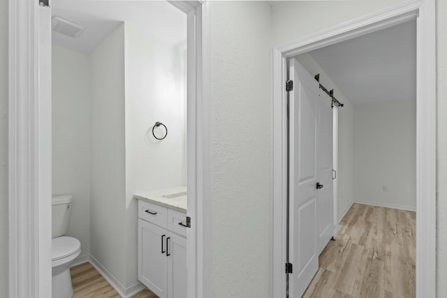 bathroom with vanity, wood finished floors, visible vents, baseboards, and toilet