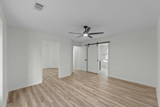 unfurnished bedroom with light wood finished floors, visible vents, baseboards, a barn door, and ensuite bathroom