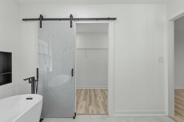 bathroom featuring a walk in closet, a soaking tub, wood finished floors, and baseboards