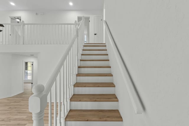 staircase featuring recessed lighting, a towering ceiling, and wood finished floors