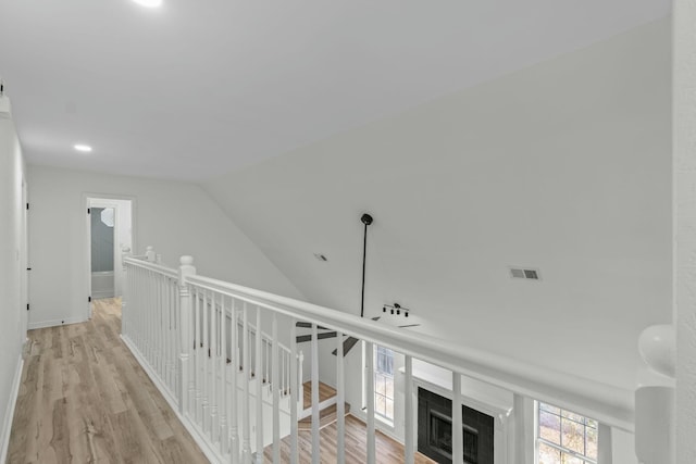 hall featuring visible vents, baseboards, wood finished floors, and vaulted ceiling