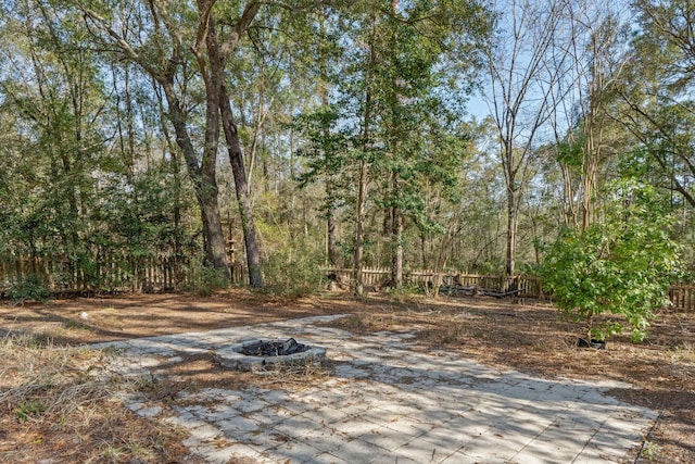 view of yard featuring a fire pit, fence, and a view of trees