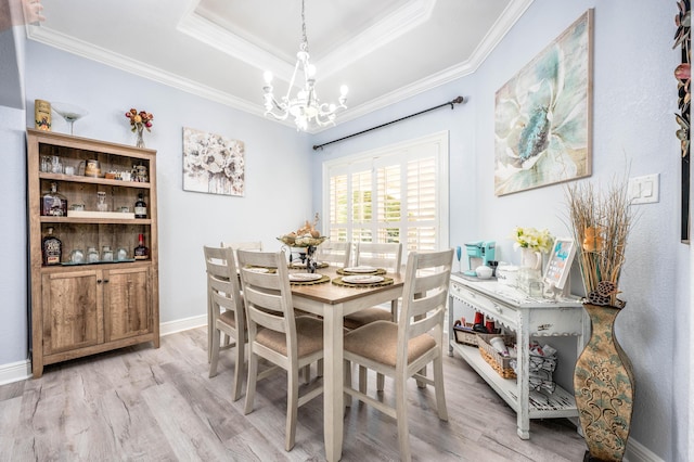 dining area with a raised ceiling, ornamental molding, light wood finished floors, baseboards, and a chandelier