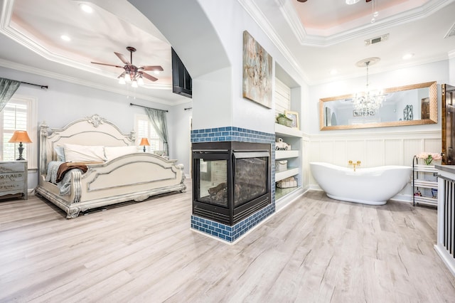 bathroom featuring crown molding, a tray ceiling, ceiling fan with notable chandelier, a tile fireplace, and a freestanding tub