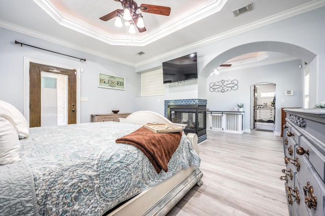 bedroom with visible vents, a tray ceiling, light wood-style flooring, arched walkways, and ornamental molding