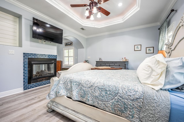 bedroom featuring wood finished floors, a tile fireplace, ceiling fan, crown molding, and a raised ceiling