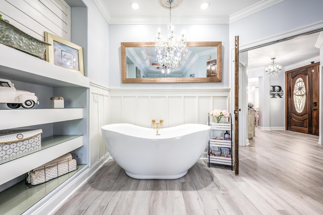 full bathroom with a chandelier, wood finished floors, ornamental molding, wainscoting, and a freestanding tub