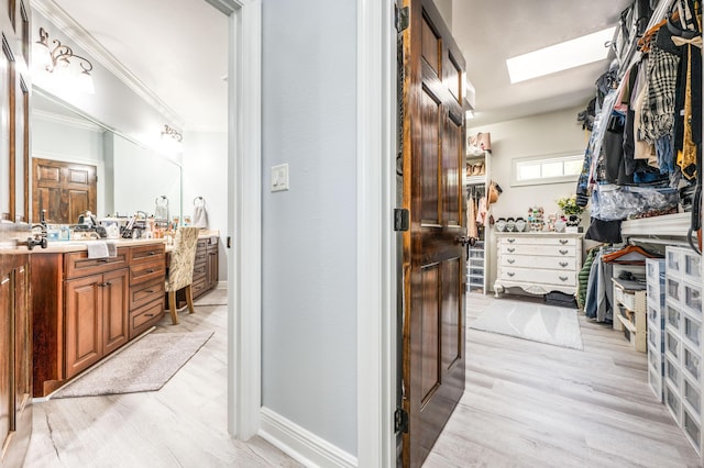 bathroom with wood finished floors, a skylight, crown molding, baseboards, and vanity