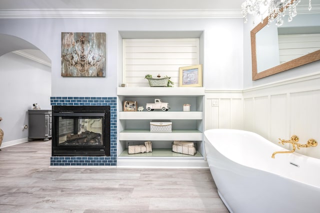 bathroom with a tiled fireplace, a soaking tub, wood finished floors, and ornamental molding