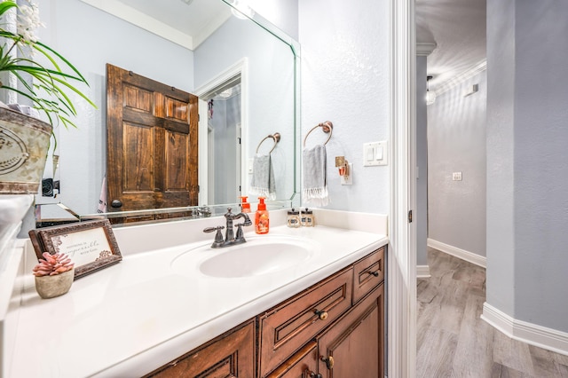 bathroom with vanity, crown molding, baseboards, and wood finished floors