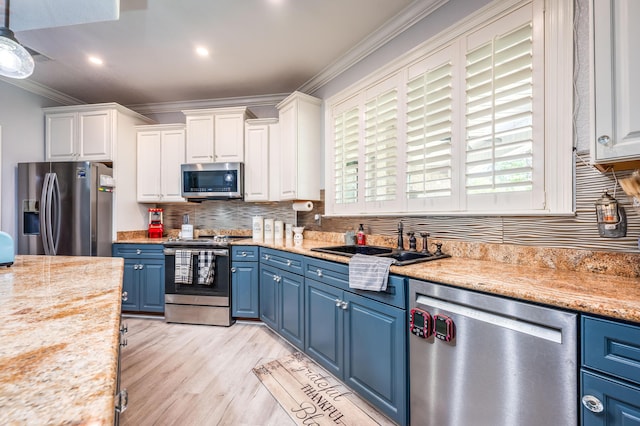 kitchen with ornamental molding, blue cabinetry, a sink, white cabinetry, and stainless steel appliances