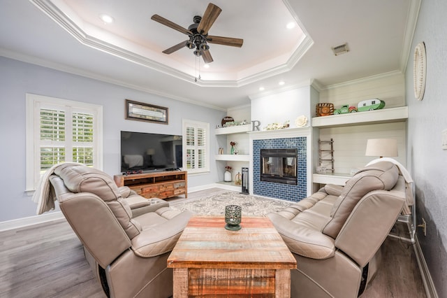 living room with wood finished floors, a raised ceiling, ceiling fan, and crown molding