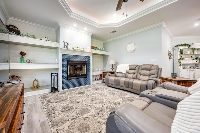 living room with visible vents, crown molding, ceiling fan, a tiled fireplace, and wood finished floors