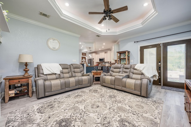 living area with a tray ceiling, a ceiling fan, visible vents, and light wood finished floors