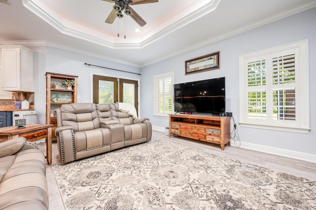 living area with a wealth of natural light, crown molding, a raised ceiling, and a ceiling fan