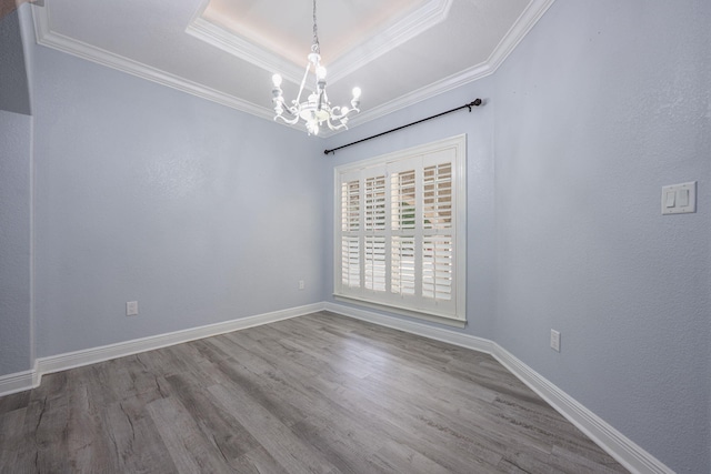 empty room featuring a tray ceiling, wood finished floors, crown molding, baseboards, and a chandelier