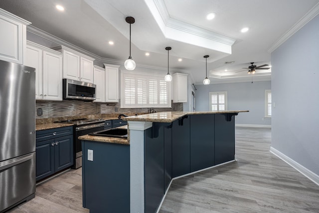 kitchen with a breakfast bar, a tray ceiling, appliances with stainless steel finishes, white cabinetry, and crown molding