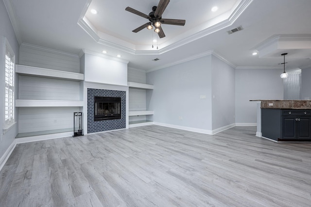 unfurnished living room with a tray ceiling, a ceiling fan, visible vents, and light wood finished floors