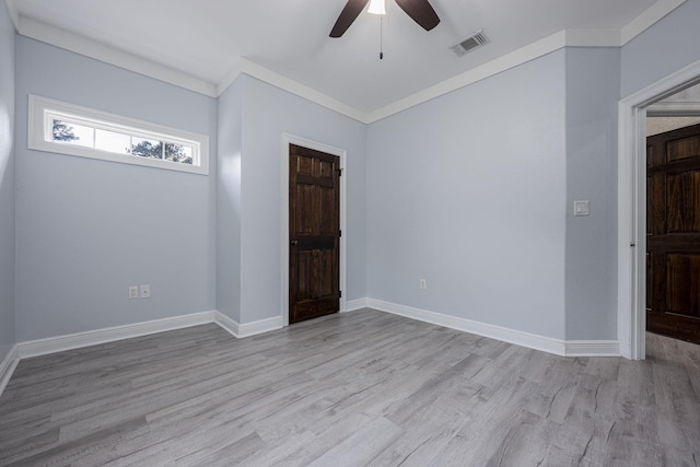 empty room with visible vents, ornamental molding, wood finished floors, baseboards, and ceiling fan