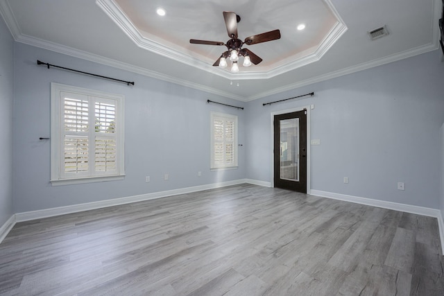 empty room with a tray ceiling, wood finished floors, a healthy amount of sunlight, and visible vents