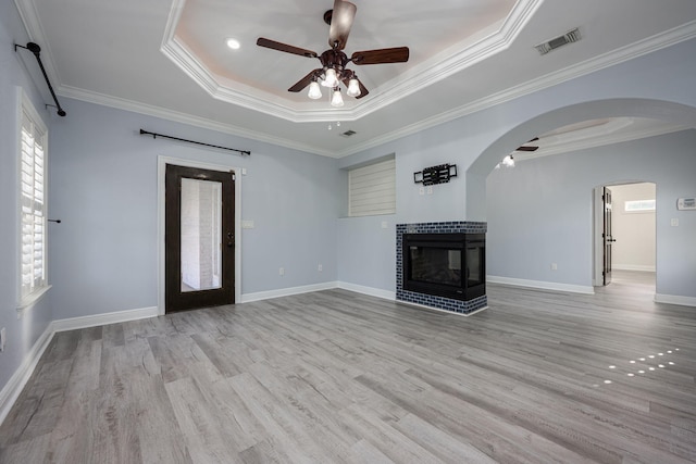 unfurnished living room with visible vents, light wood-type flooring, a ceiling fan, a tiled fireplace, and a tray ceiling