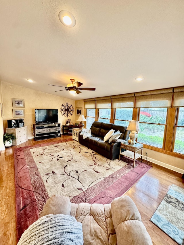 living area featuring a ceiling fan, wood finished floors, baseboards, vaulted ceiling, and a textured ceiling