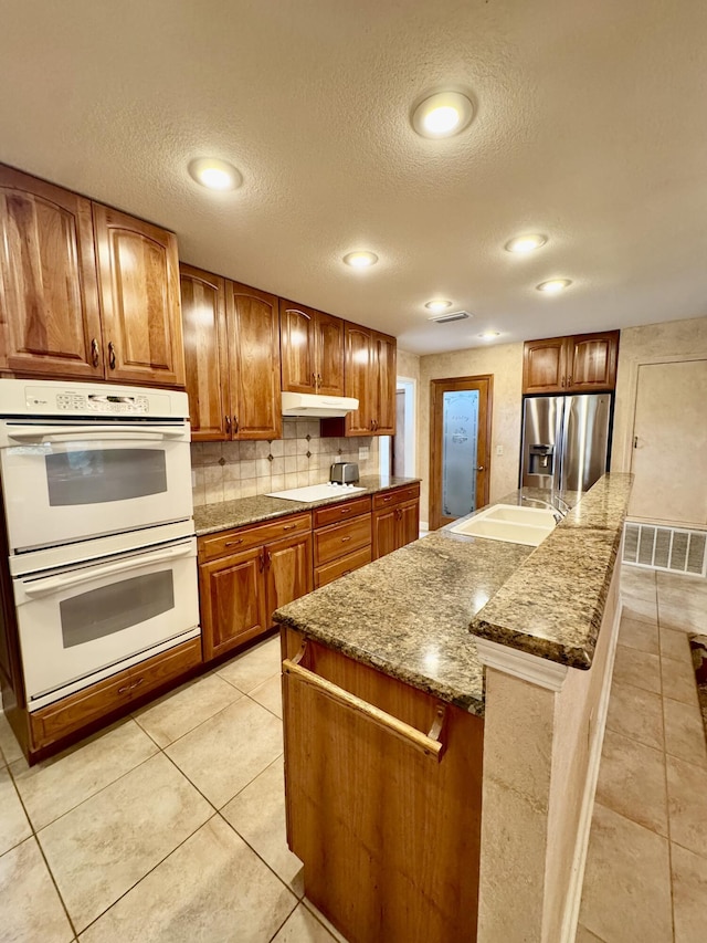 kitchen featuring a sink, under cabinet range hood, backsplash, stainless steel fridge, and white double oven