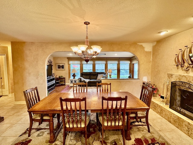 dining space featuring a high end fireplace, a textured wall, arched walkways, a notable chandelier, and a textured ceiling