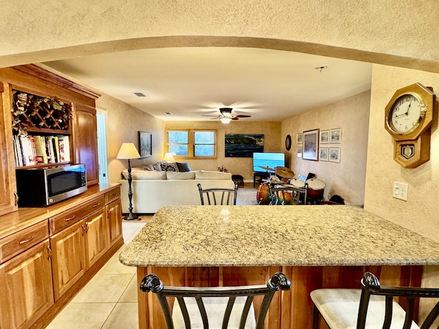 kitchen with stainless steel microwave, ceiling fan, a kitchen bar, light tile patterned floors, and a peninsula