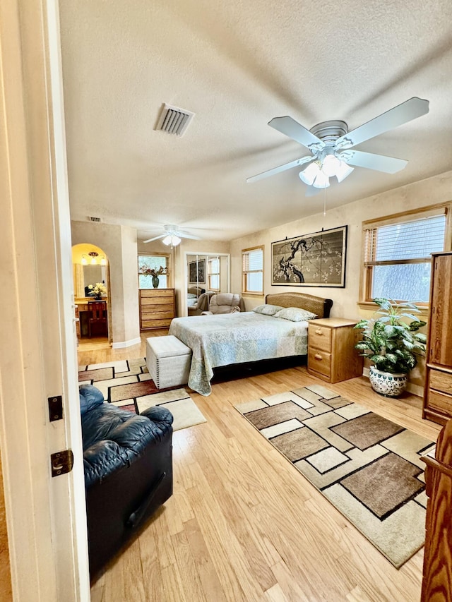 bedroom with wood finished floors, visible vents, arched walkways, ceiling fan, and a textured ceiling