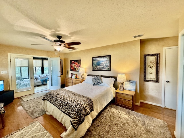 bedroom featuring access to exterior, wood finished floors, visible vents, and a textured ceiling