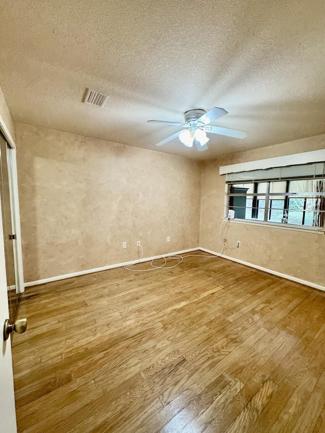 empty room featuring visible vents, a textured ceiling, wood finished floors, baseboards, and ceiling fan