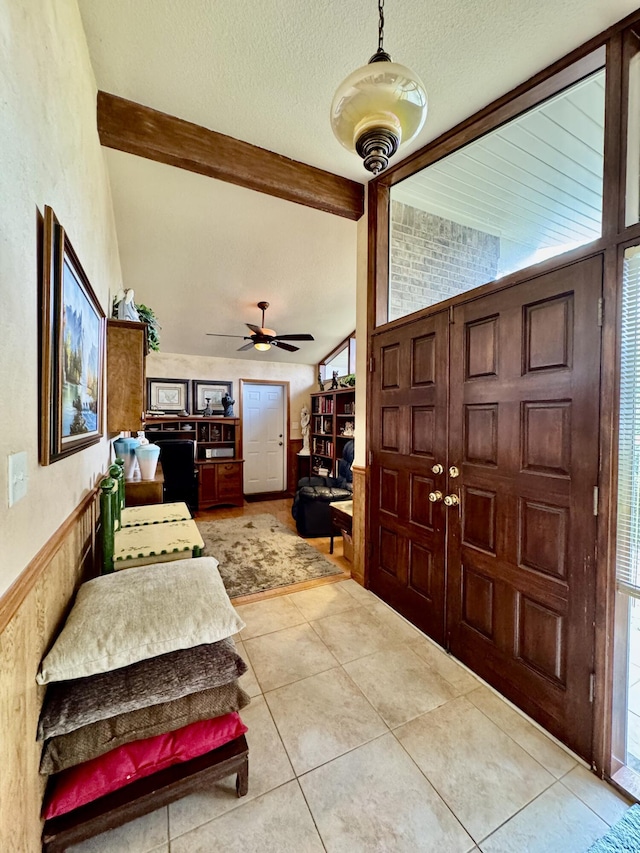 entryway with a ceiling fan, a textured ceiling, wainscoting, tile patterned flooring, and vaulted ceiling with beams