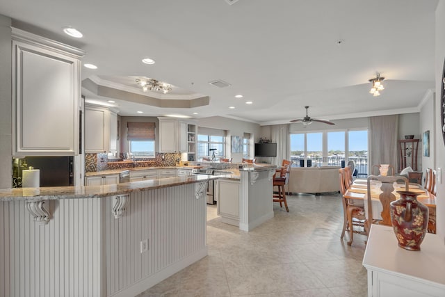 kitchen featuring visible vents, a peninsula, decorative backsplash, a raised ceiling, and a kitchen breakfast bar