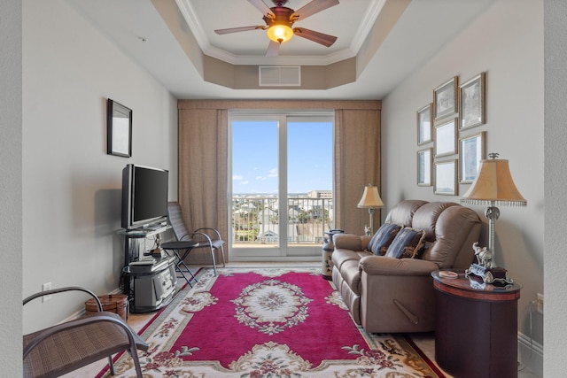 living area with visible vents, a ceiling fan, baseboards, crown molding, and a raised ceiling