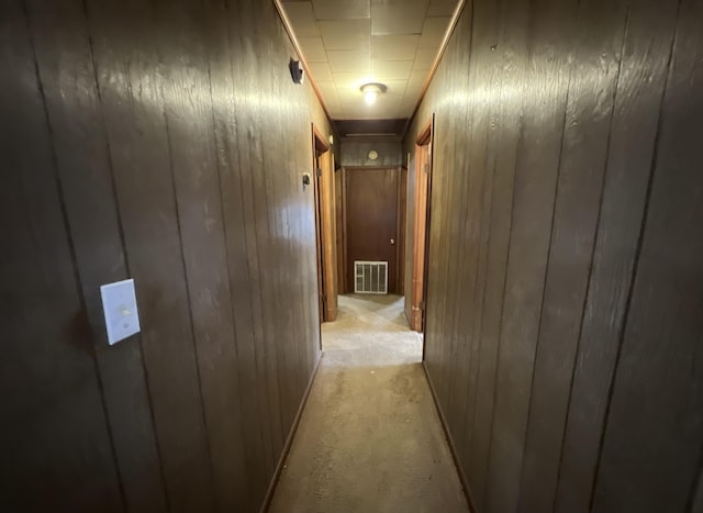 corridor with visible vents, light colored carpet, and wooden walls