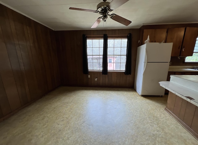 kitchen featuring light countertops, a ceiling fan, wood walls, and freestanding refrigerator