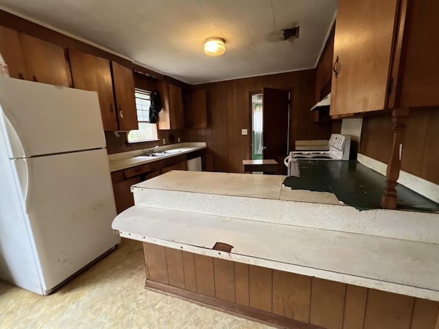 kitchen with white appliances, wooden walls, a sink, light countertops, and under cabinet range hood