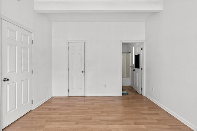 unfurnished bedroom with beam ceiling, connected bathroom, baseboards, and light wood-style floors