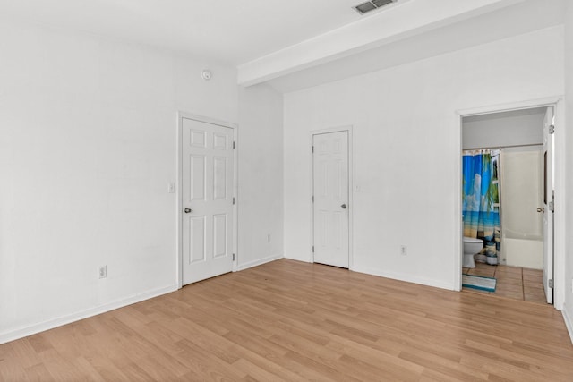 unfurnished bedroom featuring baseboards, beam ceiling, light wood-style floors, and ensuite bathroom