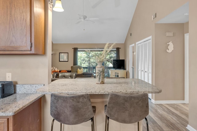 kitchen with light stone counters, visible vents, light wood-type flooring, ceiling fan, and open floor plan