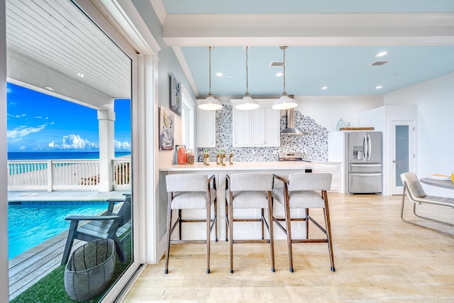 kitchen featuring light wood-type flooring, decorative backsplash, white cabinetry, wall chimney exhaust hood, and stainless steel fridge