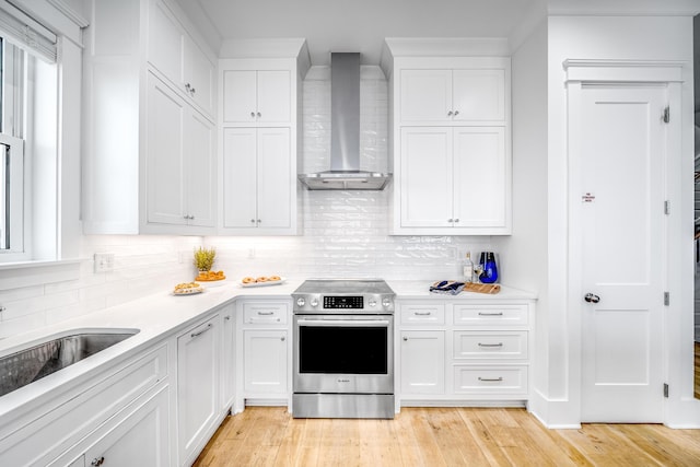 kitchen featuring wall chimney range hood, electric stove, light wood-style flooring, and white cabinets