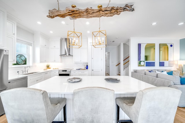 kitchen with wall chimney range hood, light countertops, an inviting chandelier, stainless steel appliances, and a sink