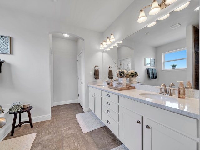 bathroom featuring baseboards, double vanity, a sink, and visible vents