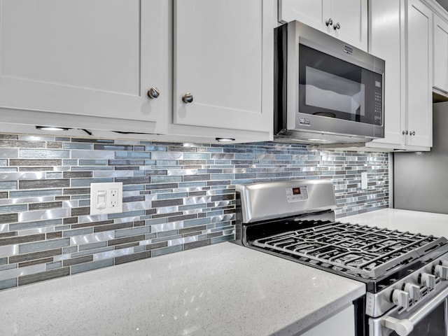 kitchen with light stone counters, backsplash, white cabinets, and stainless steel appliances