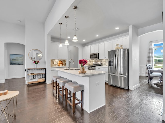 kitchen featuring arched walkways, appliances with stainless steel finishes, light countertops, and dark wood-style floors