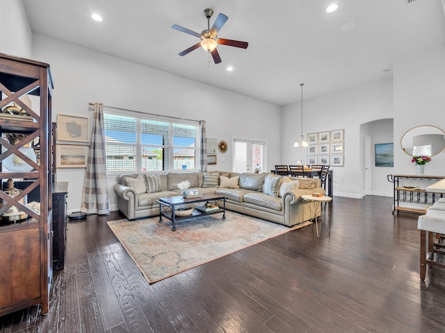 living room featuring a towering ceiling, recessed lighting, dark wood-style floors, arched walkways, and ceiling fan with notable chandelier