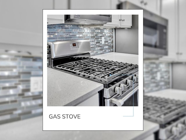 kitchen featuring tasteful backsplash, white cabinets, under cabinet range hood, stainless steel appliances, and light stone counters